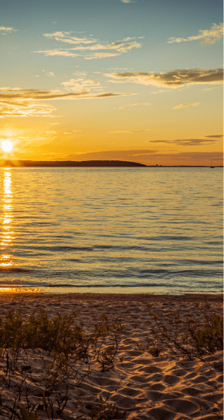 Sunset over a calm lake with sandy beach and low vegetation, capturing the natural beauty and serene outdoor adventure opportunities in Northern Michigan.
